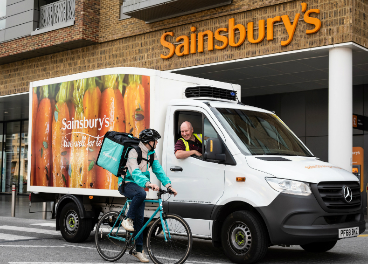 Rider de Deliveroo junto a camión de Sainsbury's